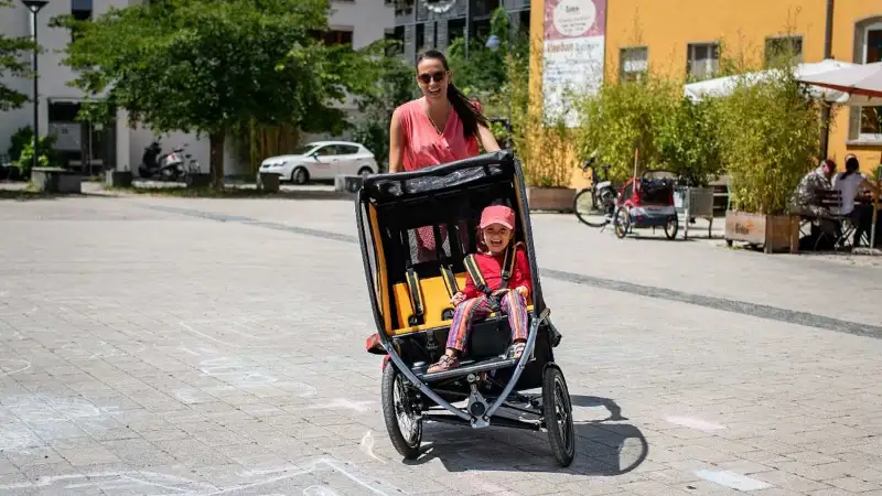 Eine Mutter fährt das Chike e-Bike in der Stadt. Ihr Kind sitzt angeschnallt darin. Beide lachen